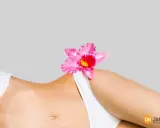 Delikatna różowa orchidea na tle kobiecego ciała, symbolizująca naturalne piękno i różnorodne rodzaje warg sromowych.