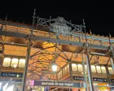 Das Mercado de San Miguel bei Nacht, mit seinem verzierten Eingang und den Lichtern, die durch das Glasdach scheinen.