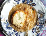Piatto di zuppa di cipolle fumante, con crostino di pane e formaggio fuso, servita su un elegante piatto decorato.
