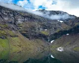 Vacker fjällsjö med en porlande vattenfall, perfekt för dagsturer i Abisko. Moln sveper över bergstopparna.