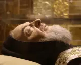 Szczątki sw. Pio w szklanej gablocie, z widocznym fragmentem twarzy, brody i zdobionego szat.