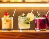 Trzy kolorowe drinki na barze: żółty z wiśnią, zielony z limonką i miętą, oraz fioletowy z pitają. Idealne do letnich wieczorów, a może i z **kazbek peak brandy z czym pić**?
