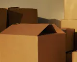 Stos kartonów, niektóre otwarte, gotowe do przeprowadzki. Różne wymiary kartonów tworzą ciekawą kompozycję.