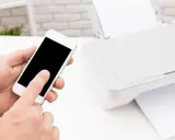Instrukcja: jak połączyć telefon z drukarką. Smartfon w dłoni, obok drukarka z papierem.