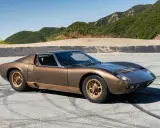 Ein brauner Lamborghini Miura S steht auf einer asphaltierten Straße mit Bergkulisse.
