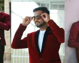 Three men sport stylish burgundy and red blazers. One adjusts his hair, another his sunglasses, and the third checks his phone.