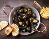 Moules marinières, une spécialité culinaire normande, servies dans une marmite en cuivre avec des frites et du pain grillé.