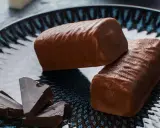 Dwa czekoladowe batony proteinowe na talerzu, obok kawałki gorzkiej czekolady. Idealne do domowego batony proteinowe przepis.