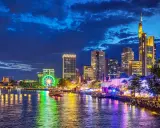 Frankfurt Mainufer bei Nacht: Lichtermeer, beleuchtetes Riesenrad und Skyline spiegeln sich im Wasser.