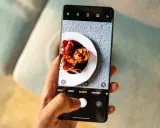 Dłoń trzyma telefon, na ekranie którego aparat robi zdjęcie pysznych ptysiów polanych czekoladą.