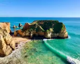 Traumhafte Felsformationen und türkisfarbenes Wasser am Praia de Alvor. Eine kleine Bucht mit Sand und grünen Klippen.