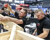Dwóch mężczyzn buduje drewnianą konstrukcję, jeden używa wkrętarki.