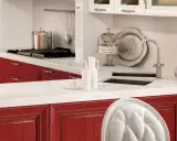 Cucina con ante rosse, piano bianco, pentola sul fornello, torta sotto campana di vetro. Okite cos'è? Un piano di lavoro resistente e bello.
