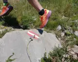 Biegacz w butach Hoka Speedgoat 6 pokonuje górski szlak, stawiając stopę na skale z oznaczeniem szlaku.