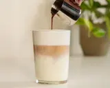 Espresso wird in ein Glas mit Milch und Milchschaum gegossen. Ein perfektes Latte Macchiato Rezept.