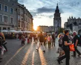 Tłum ludzi spaceruje po Rynku Głównym w Krakowie o zachodzie słońca. Widać Sukiennice i wieżę Ratuszową. Czy jest krakow safe? Tak, to tętniące życiem, bezpieczne miasto.