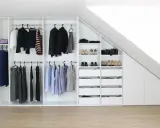 Ein maßgefertigter Kleiderschrank bauen, der sich perfekt in die Dachschräge einfügt. Ordentlich sortierte Kleidung und Schuhe.