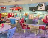 Interni di un diner in **stile americano** con sedili color pastello, tavoli cromati e decorazioni a tema auto d'epoca.