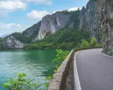 Strada panoramica lungo un lago verde smeraldo, con imponenti pareti rocciose e vegetazione lussureggiante. Un percorso suggestivo per raggiungere la baia di Bogn.