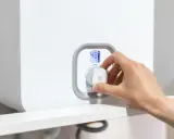 Mano ajustando el dial de una caldera para bajar la presión. La pantalla digital muestra 48°C.