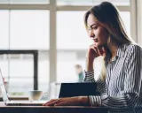 Donna pensa a come fare un webinar, seduta al laptop con una tazza di caffè.
