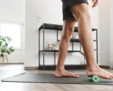 Mann rollt mit einem kleinen grünen Ball unter dem Fuß, um Plantarfasziitis-Hausmittel anzuwenden.