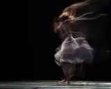 Danzatrice eterea catturata in una foto in movimento Android, con un abito svolazzante e capelli che sembrano fumo su sfondo nero.