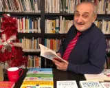 Daniele Novara, autore di libri per genitori, legge un suo libro tra scaffali pieni di volumi, con un albero di Natale e una bottiglia di spumante.