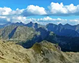 Widok z Zawratu na skaliste szczyty Tatr pod błękitnym niebem z białymi chmurami.