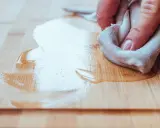 Mano limpiando pintura del suelo de madera con un trapo.