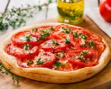 Tarte aux tomates cerises, garnie d'herbes fraîches et d'ail, prête à être dégustée.