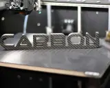 Ein 3D-Drucker fertigt das Wort "CARBON" aus einer Carbonplatte.