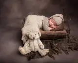 Dolce bimbo appena nato dorme sereno in una culla con un orsacchiotto. Foto bimbi appena nati.