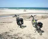 Dwa rowery z sakwami na piaszczystej plaży, gotowe na odkrywanie płaskich tras rowerowych nad morzem.