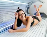Uśmiechnięta kobieta w solarium, gotowa na idealną opaleniznę. Efekt solarium przed i po to jej cel.