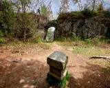 Kamienny postument przed łukiem w fort karola. Ścieżka prowadzi przez zarośla do zabytkowej budowli.
