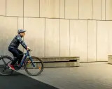 Mężczyzna w kasku i kamizelce jedzie na rowerze typu fitness w miejskim otoczeniu.