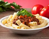 Pyszny makaron włoski rigatoni z sosem bolognese i świeżą bazylią, obok dojrzałe pomidory.