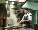 Deux chefs travaillent dans une cuisine de restaurant, respectant la norme de qualité. Vapeur s'échappant des casseroles.