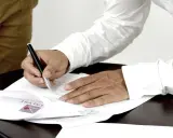 Mężczyzna podpisuje dokumenty, stając się ubezpieczającym dla ubezpieczonego. Na papierze widoczne logo firmy.
