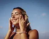 Donna sorridente applica crema solare per proteggere la pelle da macchie e tumore.
