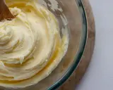 Une cuillère en bois mélange une crème au beurre traditionnelle onctueuse dans un bol en verre.