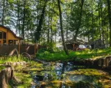Leśna polana z drewnianymi budowlami i stawem. Idealne romantyczne miejsce dla dwojga, otoczone zielenią i spokojem.