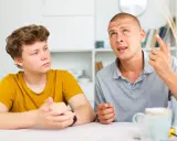 Ojciec tłumaczy synowi, jak rozmawiać z nastolatkiem, używając gestów. Chłopak słucha uważnie.