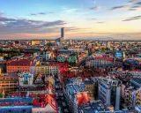 Widok na Wrocław, największe miasto zachodniej Polski, z dominującym wieżowcem Sky Tower. Słońce zachodzi nad kolorowymi dachami kamienic.