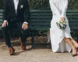 Para młoda siedzi na ławce, trzymając bukiet. To piękny obraz tego, co to jest ślub.