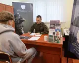 Młody mężczyzna rozmawia z żołnierzem w punkcie rekrutacyjnym. Dyskutują o możliwościach związanych z obowiązkową służbą wojskową.