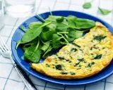 Frittata di spinaci dorata su piatto blu, accompagnata da spinacini freschi. Un pasto leggero e gustoso.