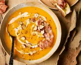 Velouté de courge onctueux, garni de noisettes croquantes, d'une touche de crème et d'une tranche de bacon croustillant. Un délice automnal qui évoque le beurre de courge.