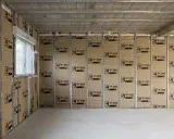 Le chantier progresse, on commence à isoler un mur avec des panneaux Isover. Une fenêtre est visible sur la gauche.
